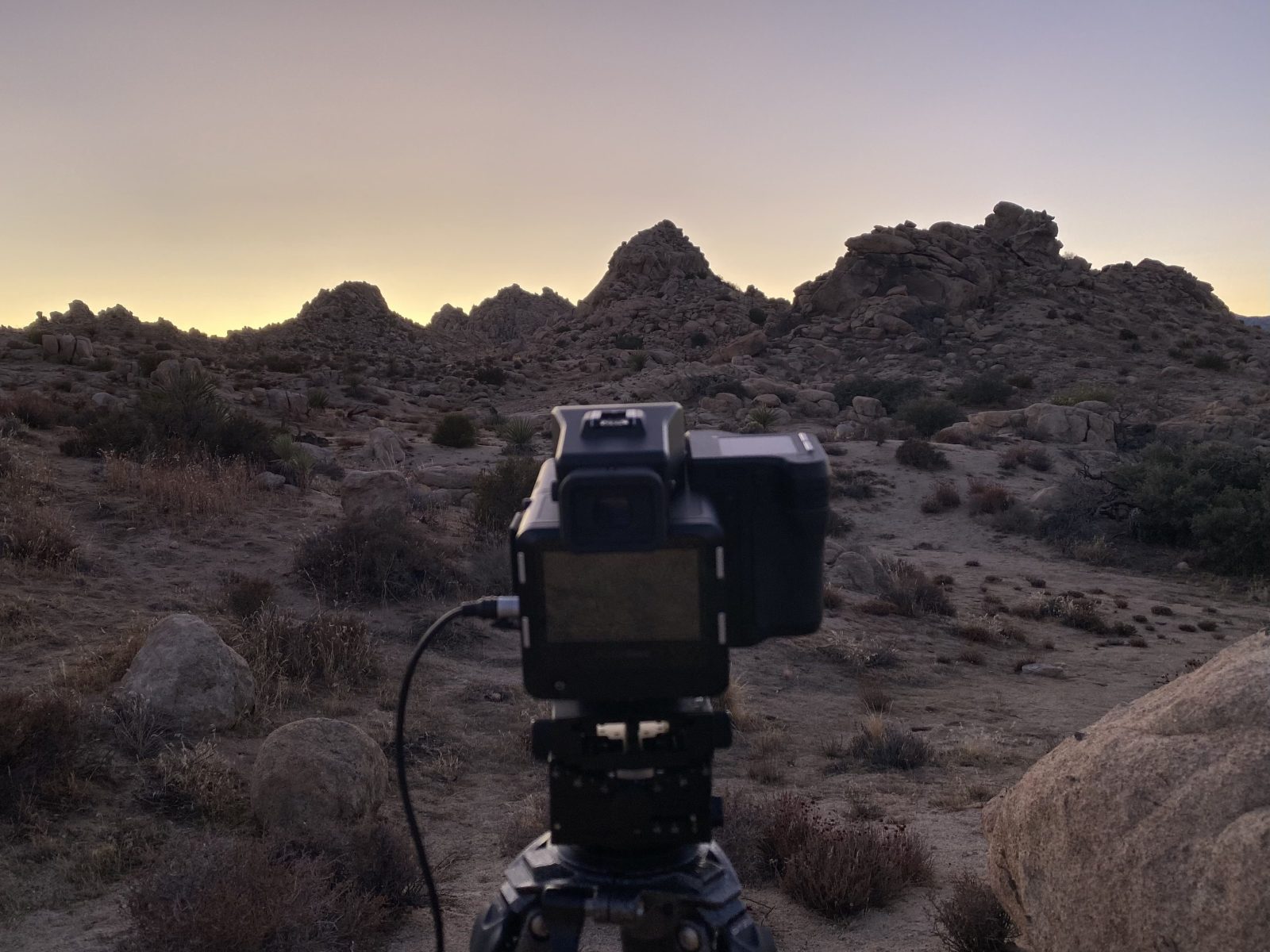 A photographer sets a camera on a tripod, capturing rocky hills at dusk in the desert landscape.