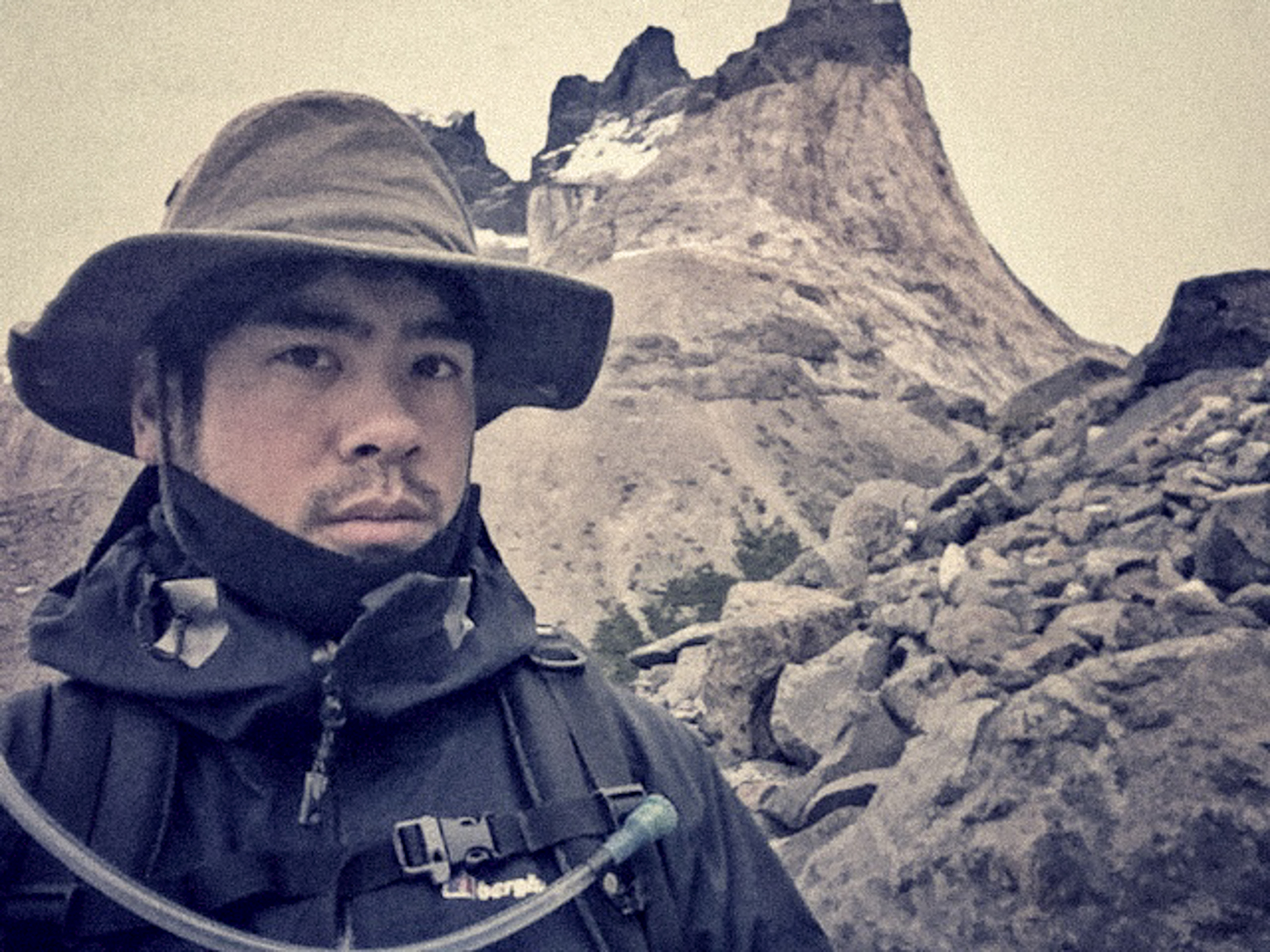 Person in outdoor gear with a wide-brim hat, standing on rocky terrain with mountains in the background—perfect inspiration for a fine artist seeking striking nighttime landscape photography.