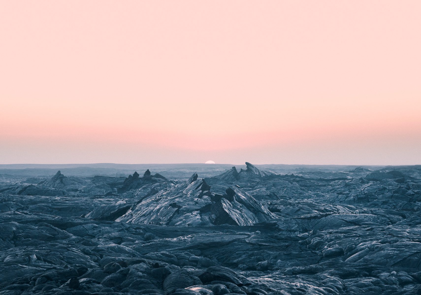 Rocky landscape with jagged peaks under a pink sky at sunrise or sunset, sun on the horizon, illuminated by futuristic drone light painting that adds a surreal glow—like a fine artist reimagining nature’s drama.
