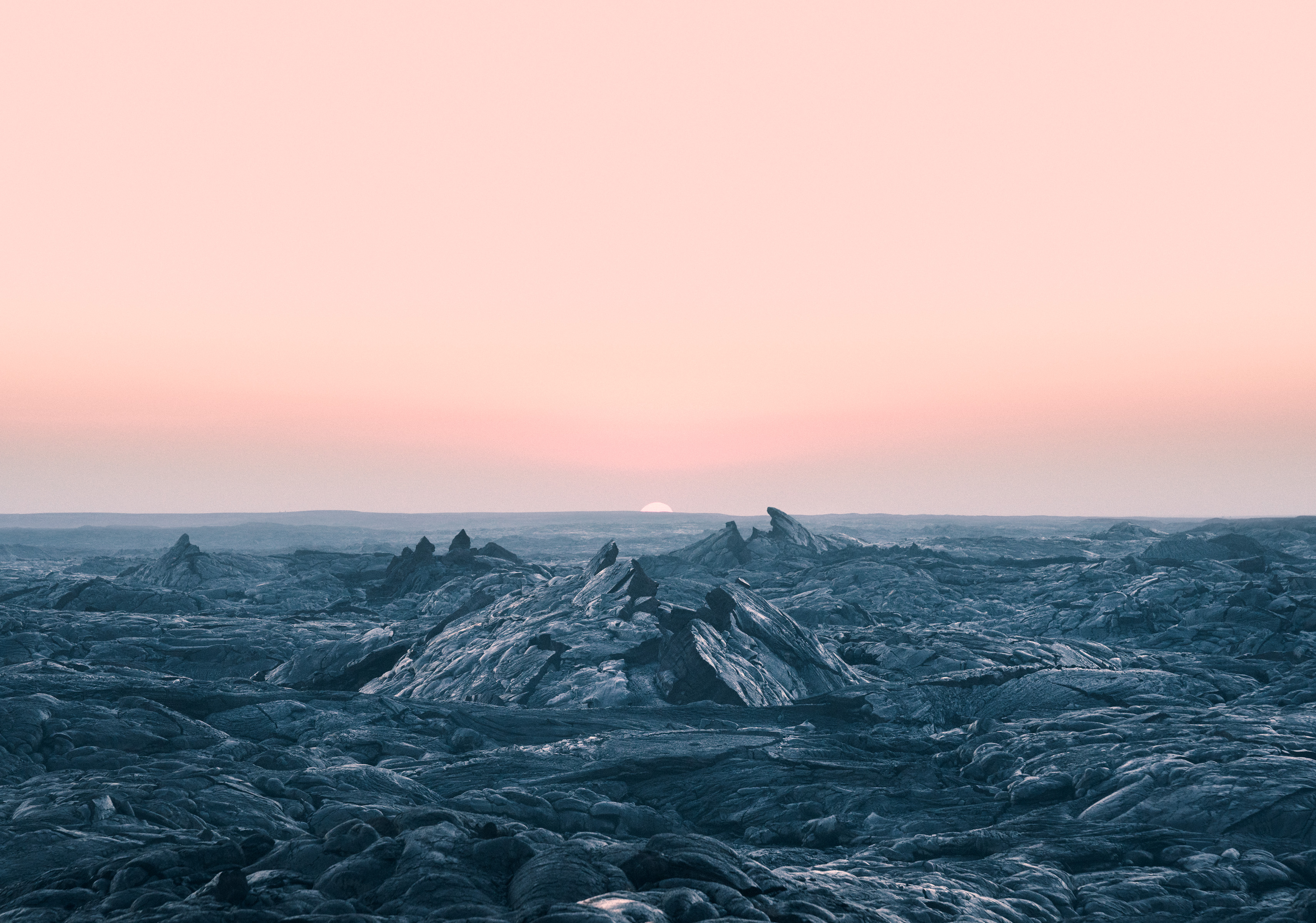 Rocky landscape with jagged peaks under a pink sky at sunrise or sunset, sun on the horizon, illuminated by futuristic drone light painting that adds a surreal glow—like a fine artist reimagining nature’s drama.