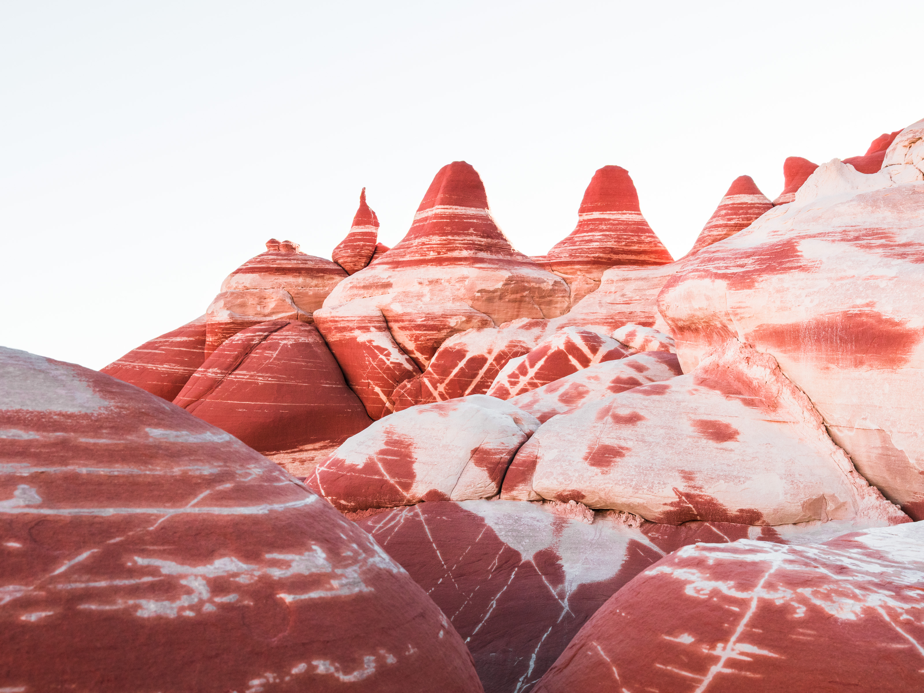 Red and white layered rock formations with rounded peaks rise beneath a clear, pale sky—an inspiring scene for any fine artist or photographer seeking unique natural beauty.
