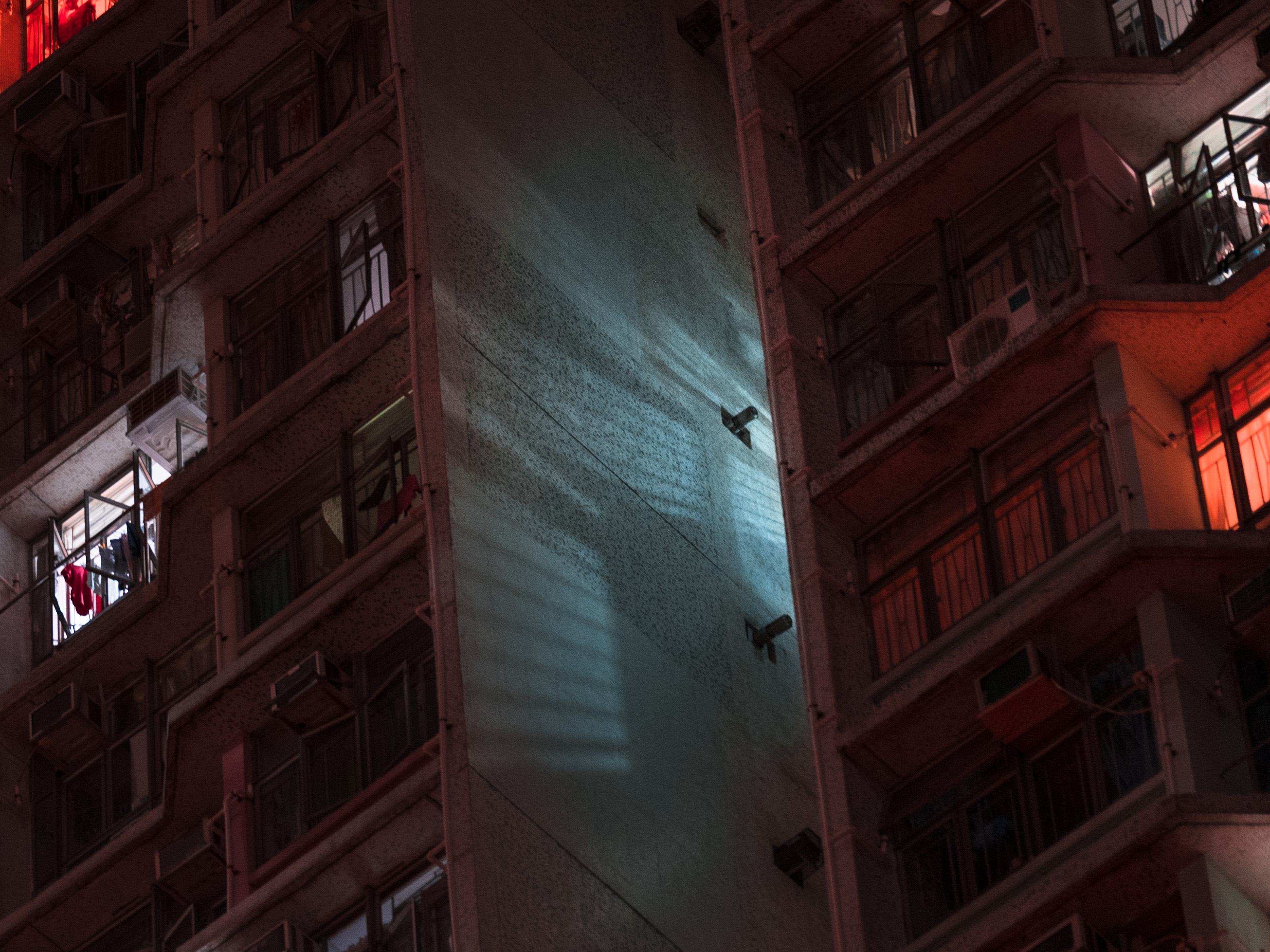 Futuristic night view of apartment balconies, with blue and red light reflecting on the building’s central wall, evoking the allure of nighttime landscape photography.