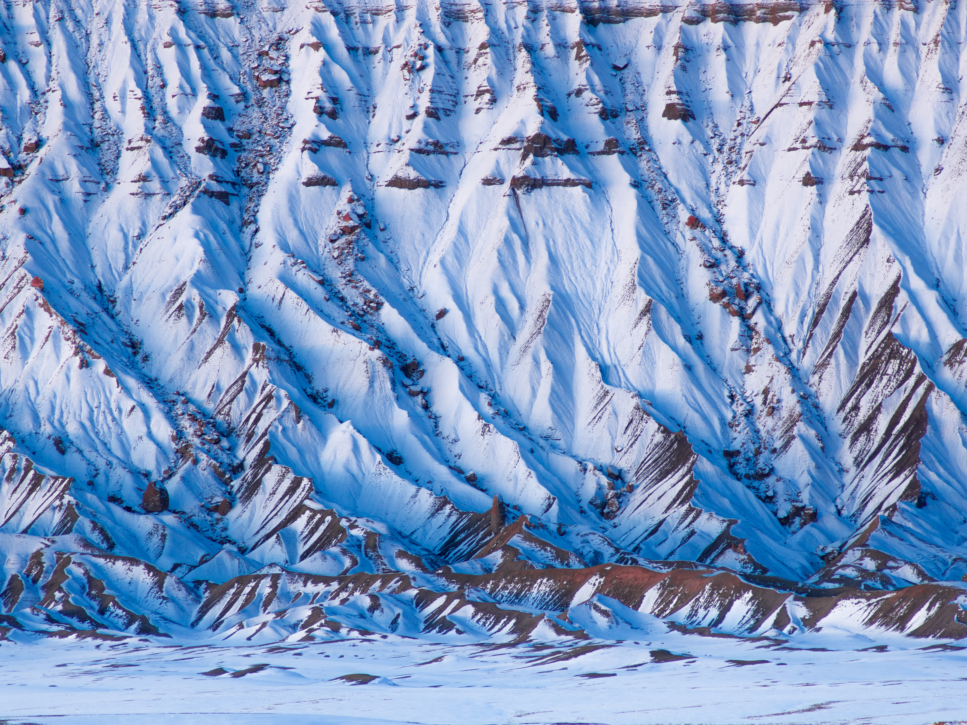 Snow-covered, steep ridges and valleys create abstract patterns on a rugged mountain landscape, perfect for nighttime landscape photography by a fine artist.