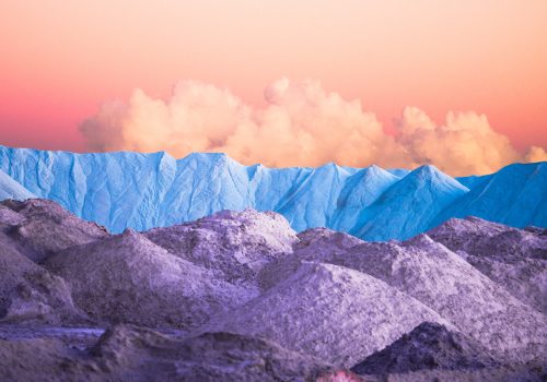 Lavender-hued hills and blue mountains under a pastel orange sky with fluffy clouds at sunset, captured by a photographer using drone light painting for a touch of futuristic artistry.