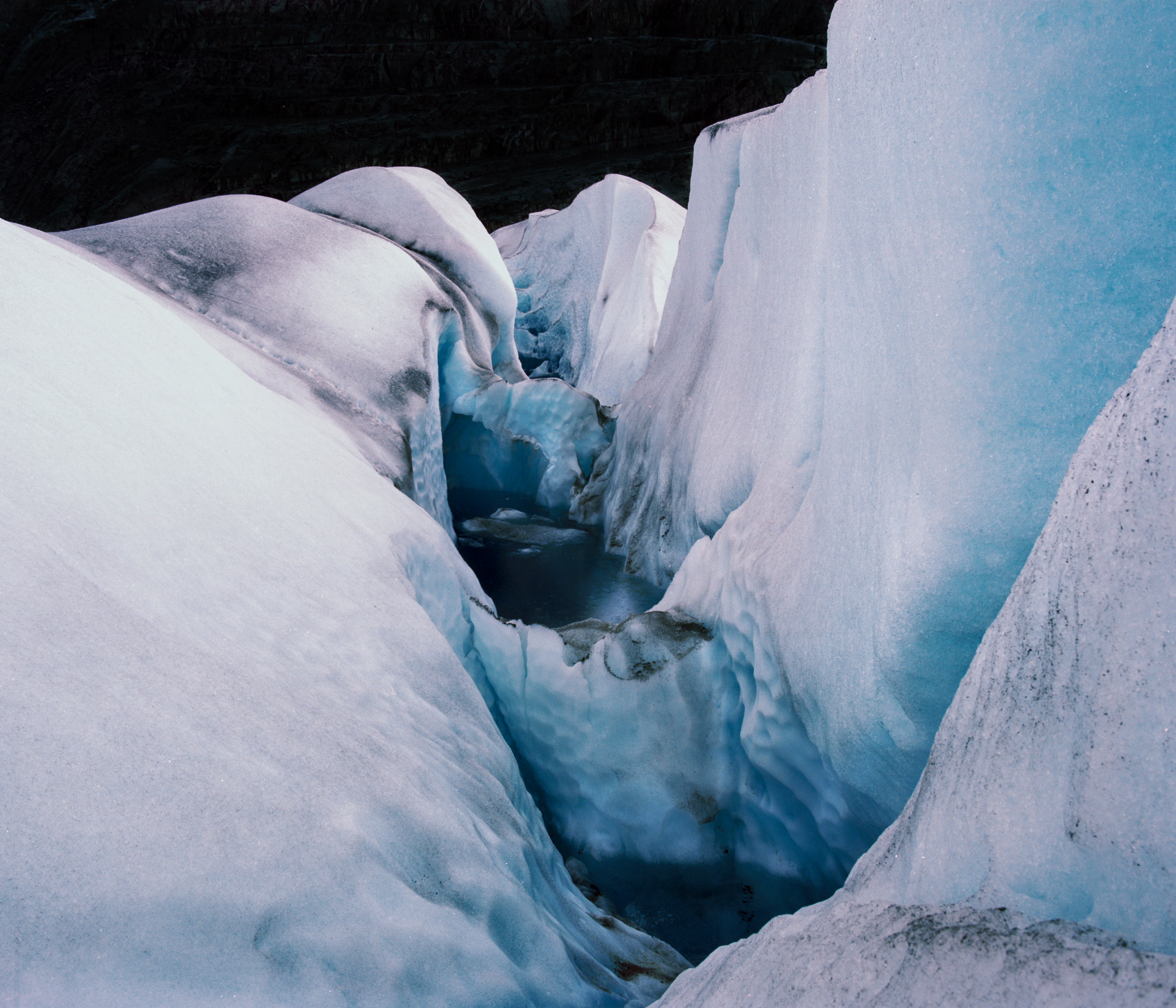 Close-up view of deep blue crevasses in a glacier, with ice walls on both sides, illuminated by futuristic drone light art.