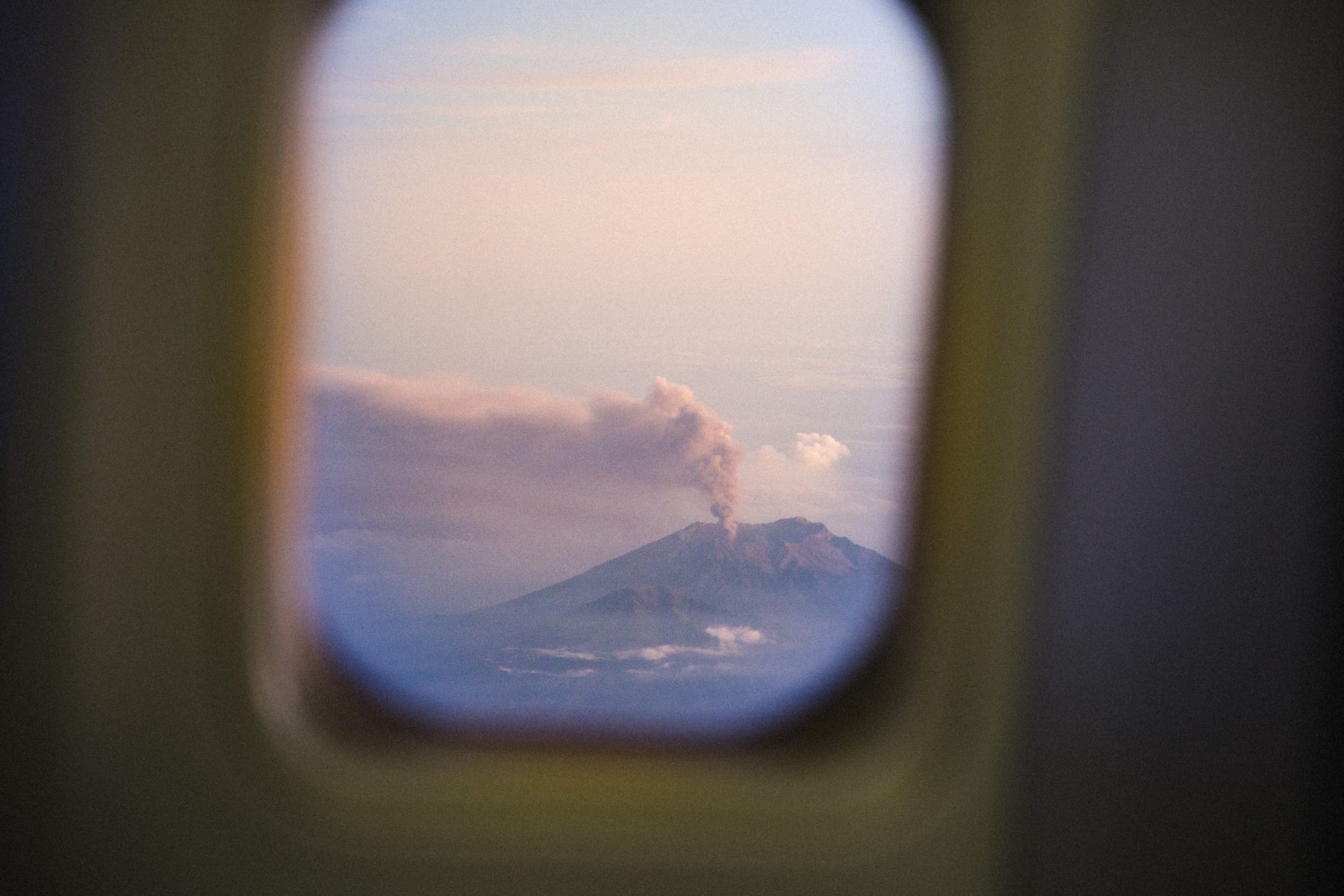 A volcano emitting smoke, seen through an airplane window during daylight hours, offers a breathtaking view that would inspire any photographer.