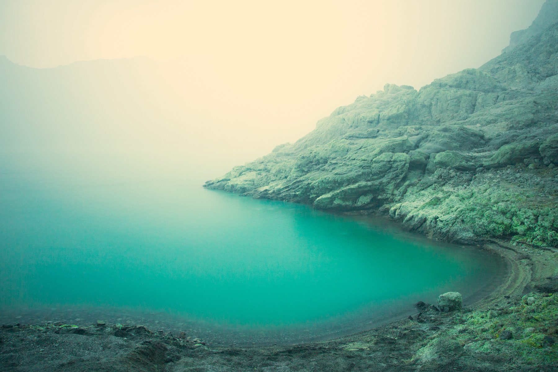 Turquoise lake surrounded by rocky cliffs under a misty, overcast sky, captured with the eye of a fine artist and the skill of a photographer.