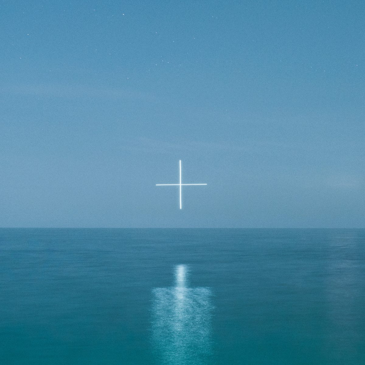 A glowing white plus sign floats above a calm blue ocean under a clear sky at dusk, creating a futuristic scene reminiscent of drone light art.