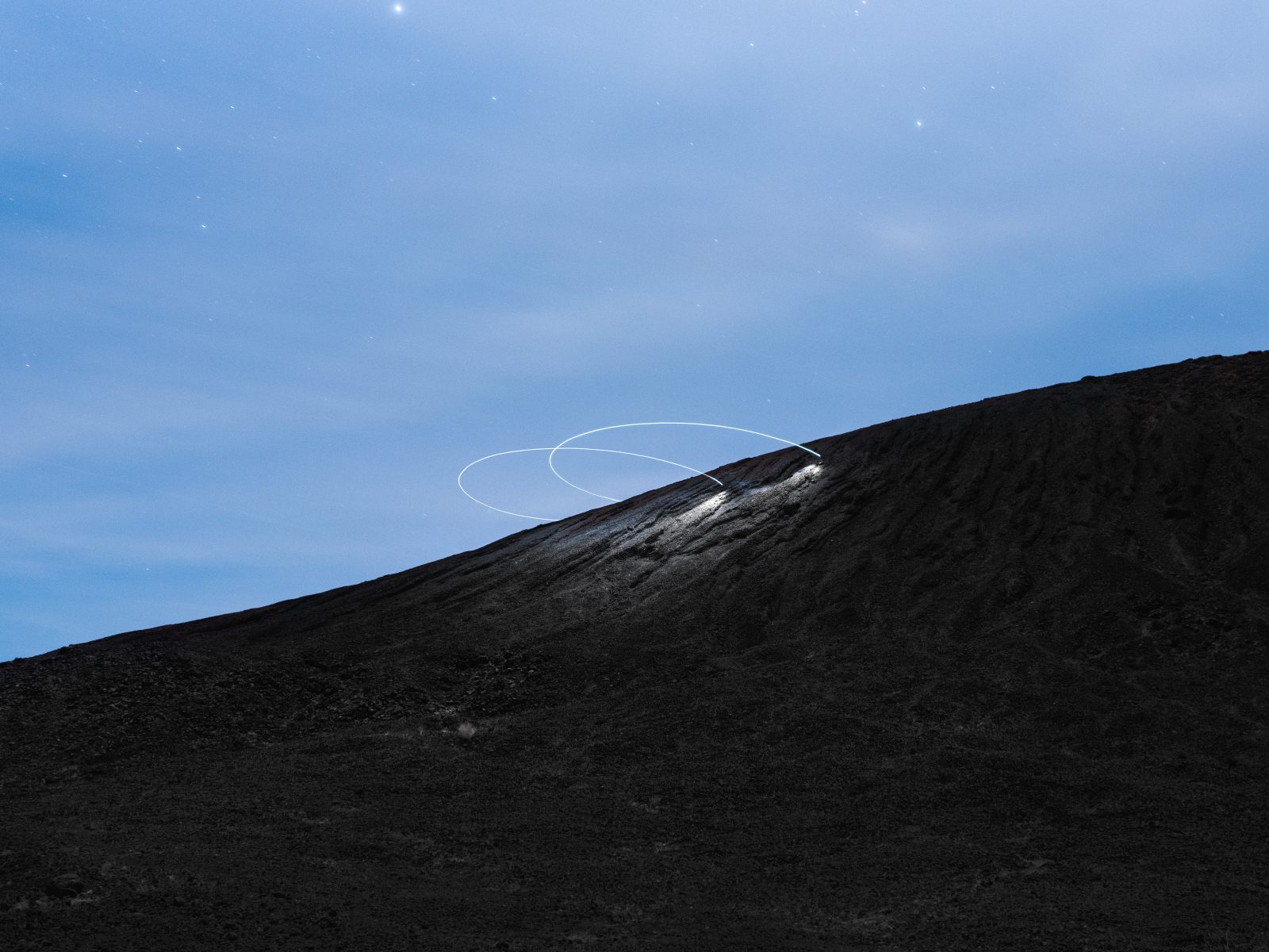 A rocky hillside under a night sky with futuristic drone light art swirling above the ridge.