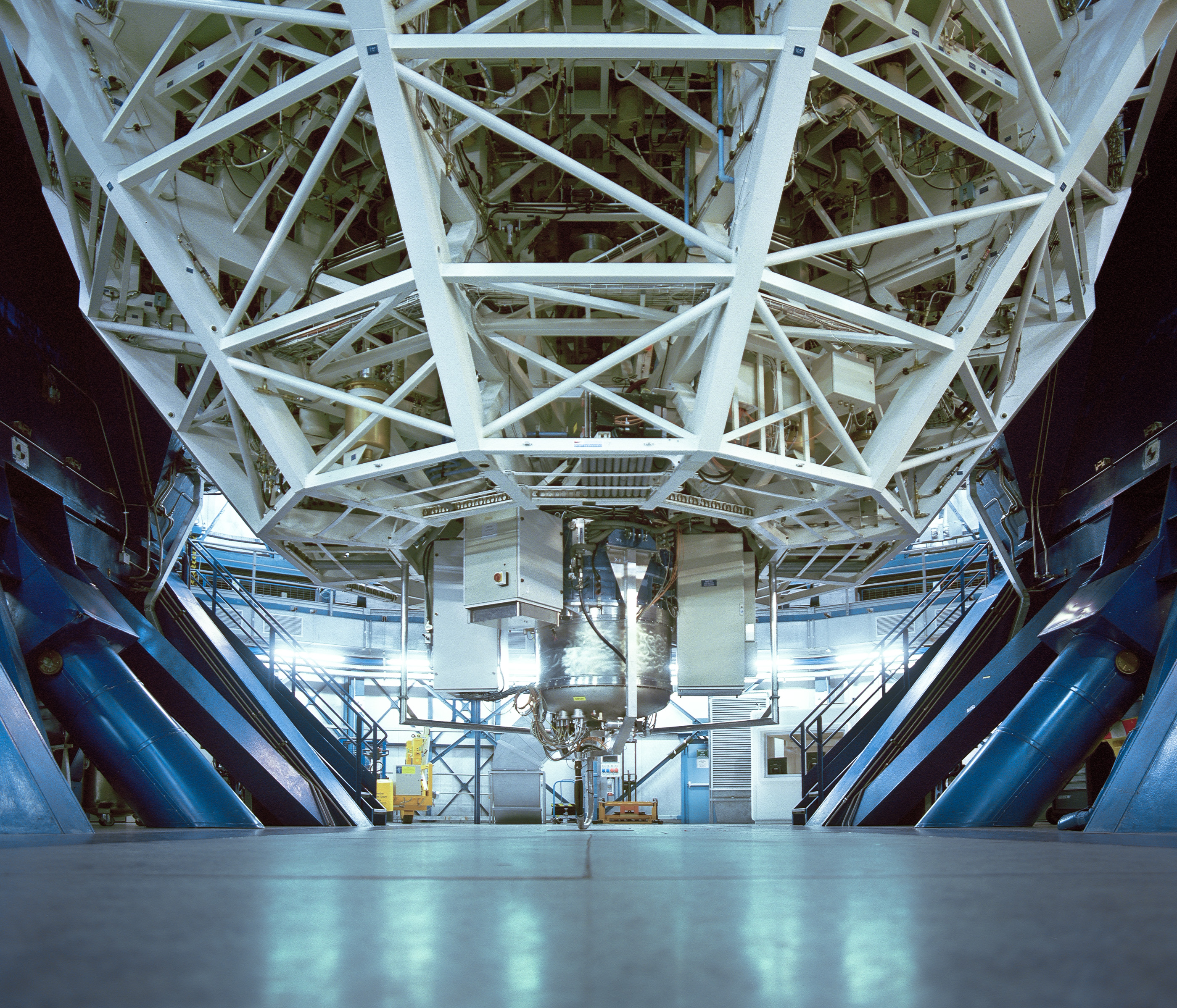 A large telescope's base and support structure inside a brightly lit observatory, reminiscent of a fine artist’s studio poised for nighttime landscape photography.