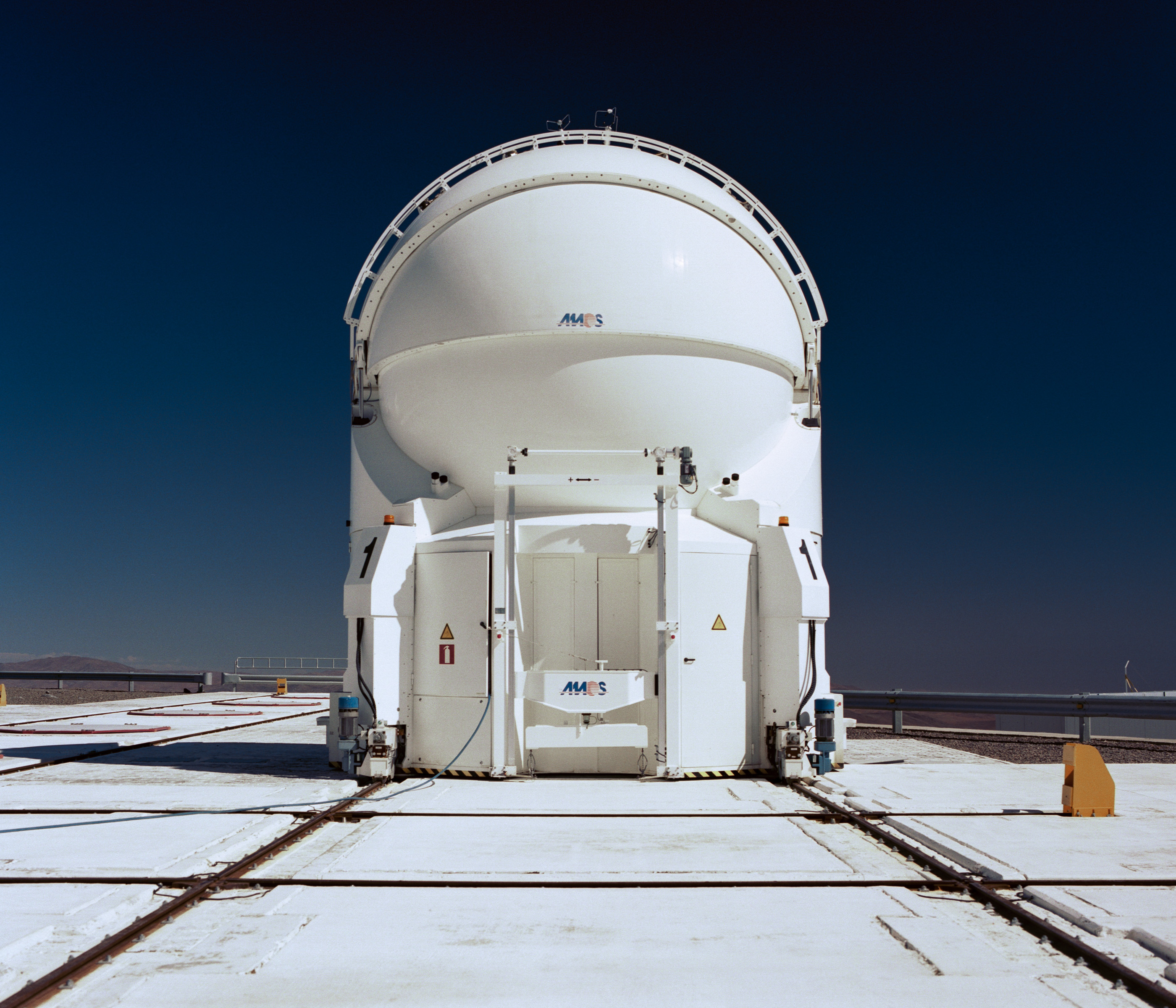 A large white telescope dome under a clear blue sky, with tracks on the ground leading up to it—a futuristic scene perfect for drone light painting displays.