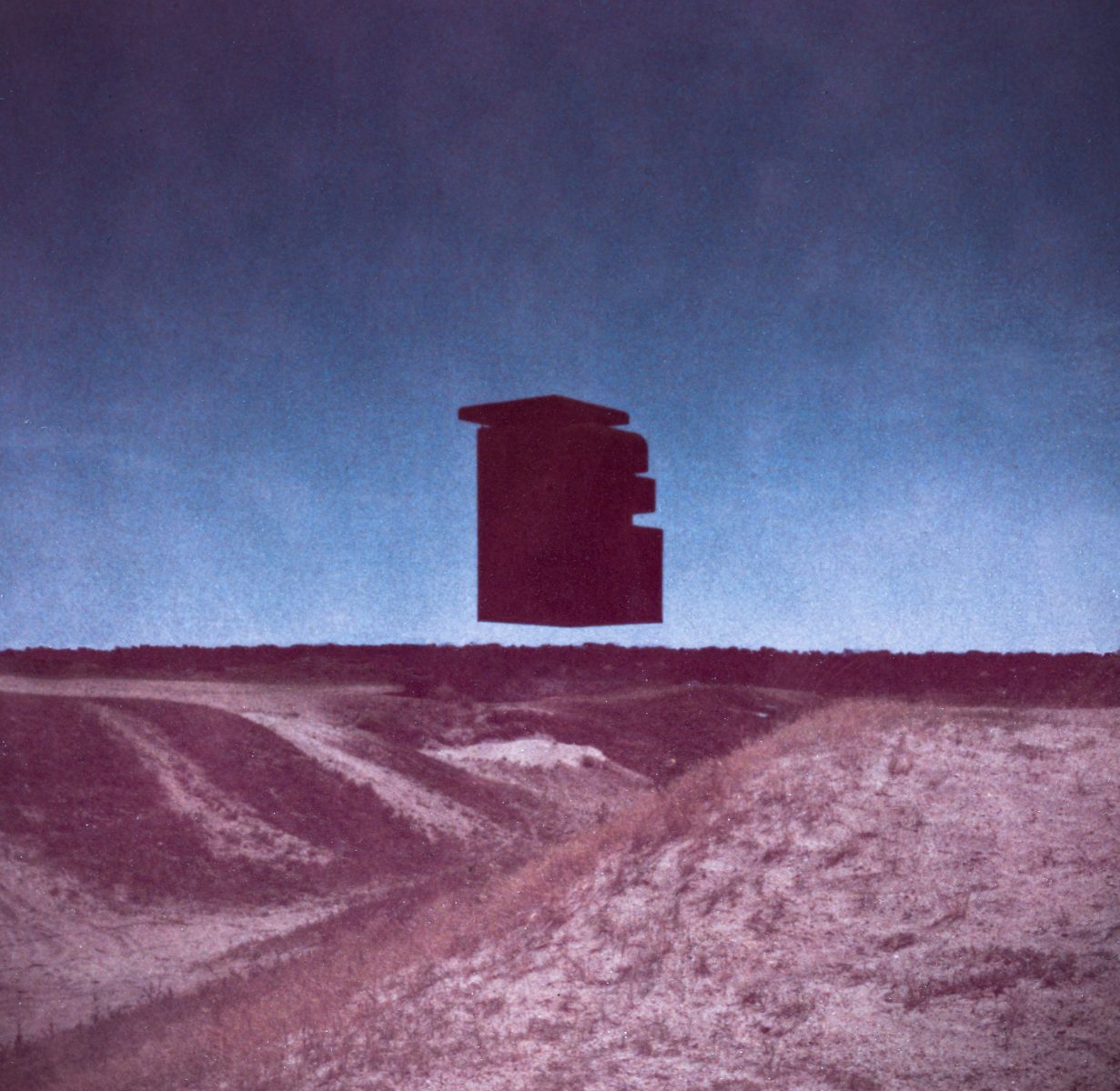 A dark, geometric structure floats above a barren, grassy landscape under a blue sky, as if captured by a photographer experimenting with drone light painting.