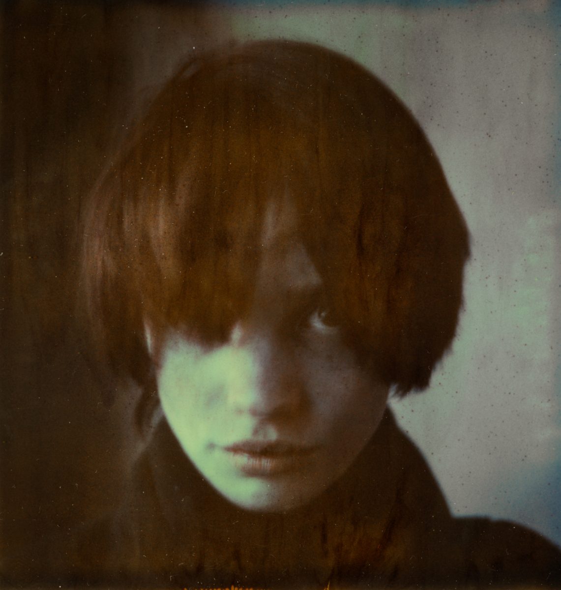 A person with short, messy hair stares intently at the camera in a dimly lit, moody portrait, evoking the mysterious allure of futuristic nighttime landscape photography.