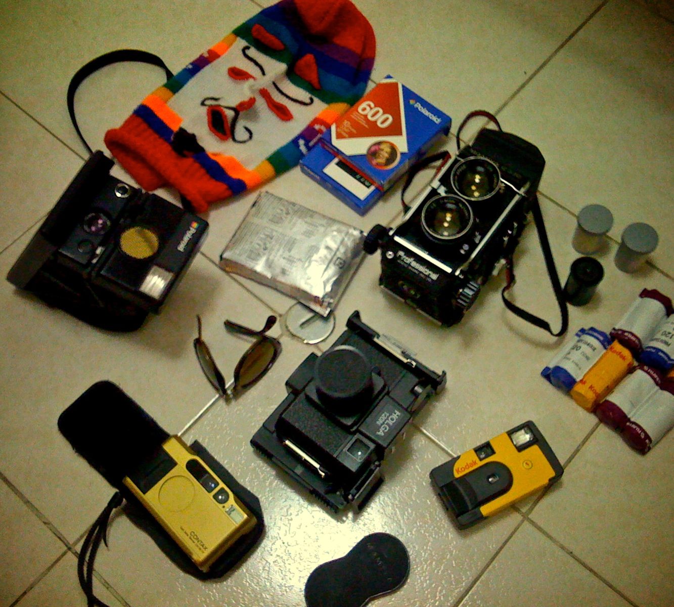 Various vintage cameras, film rolls, sunglasses, and a colorful mask arranged on a tiled floor—perfect inspiration for any fine artist or photographer drawn to unique compositions.