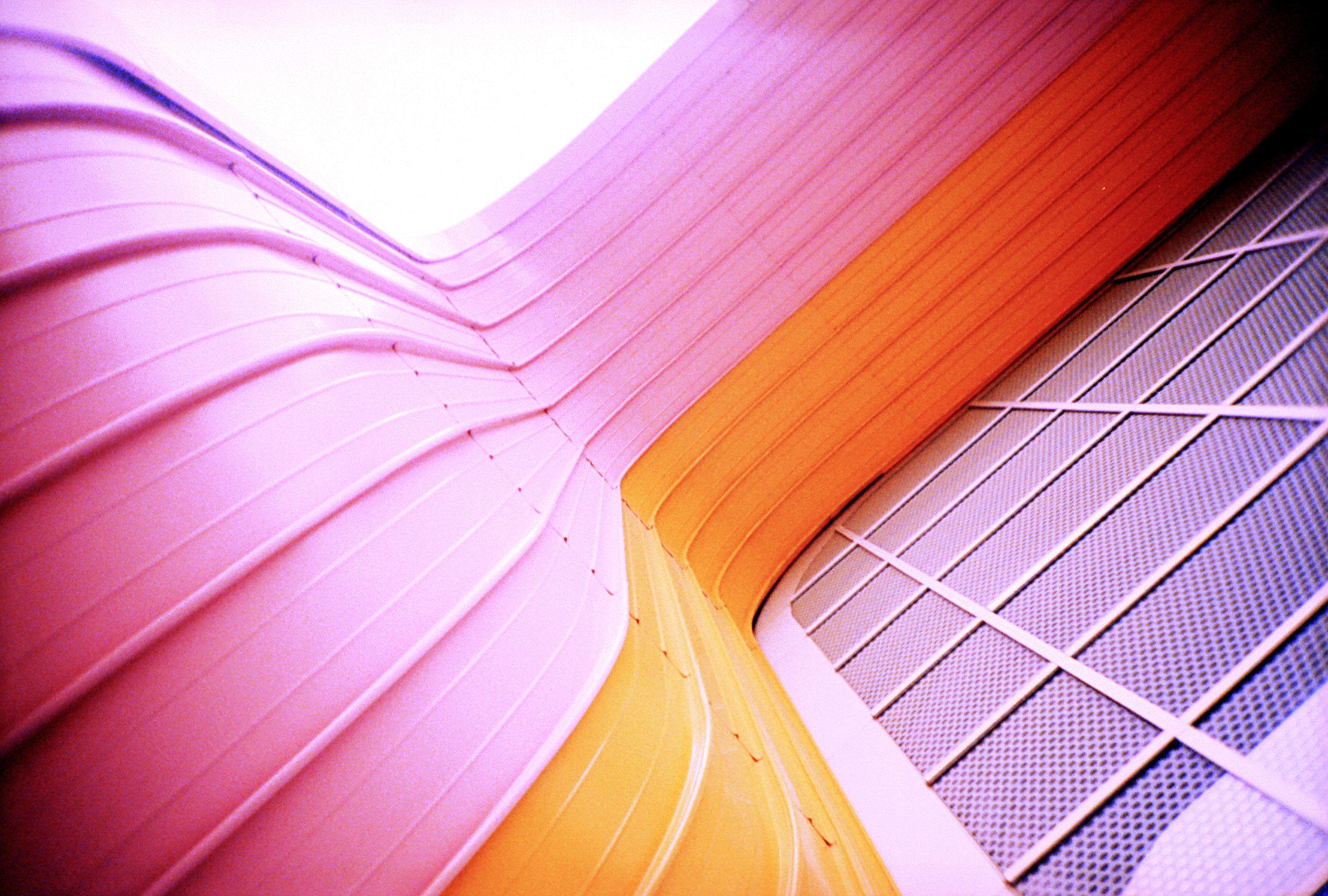 Curved pink and yellow architectural structure next to a metal grid, viewed from below—evoking the dynamic shapes often seen in drone light art.