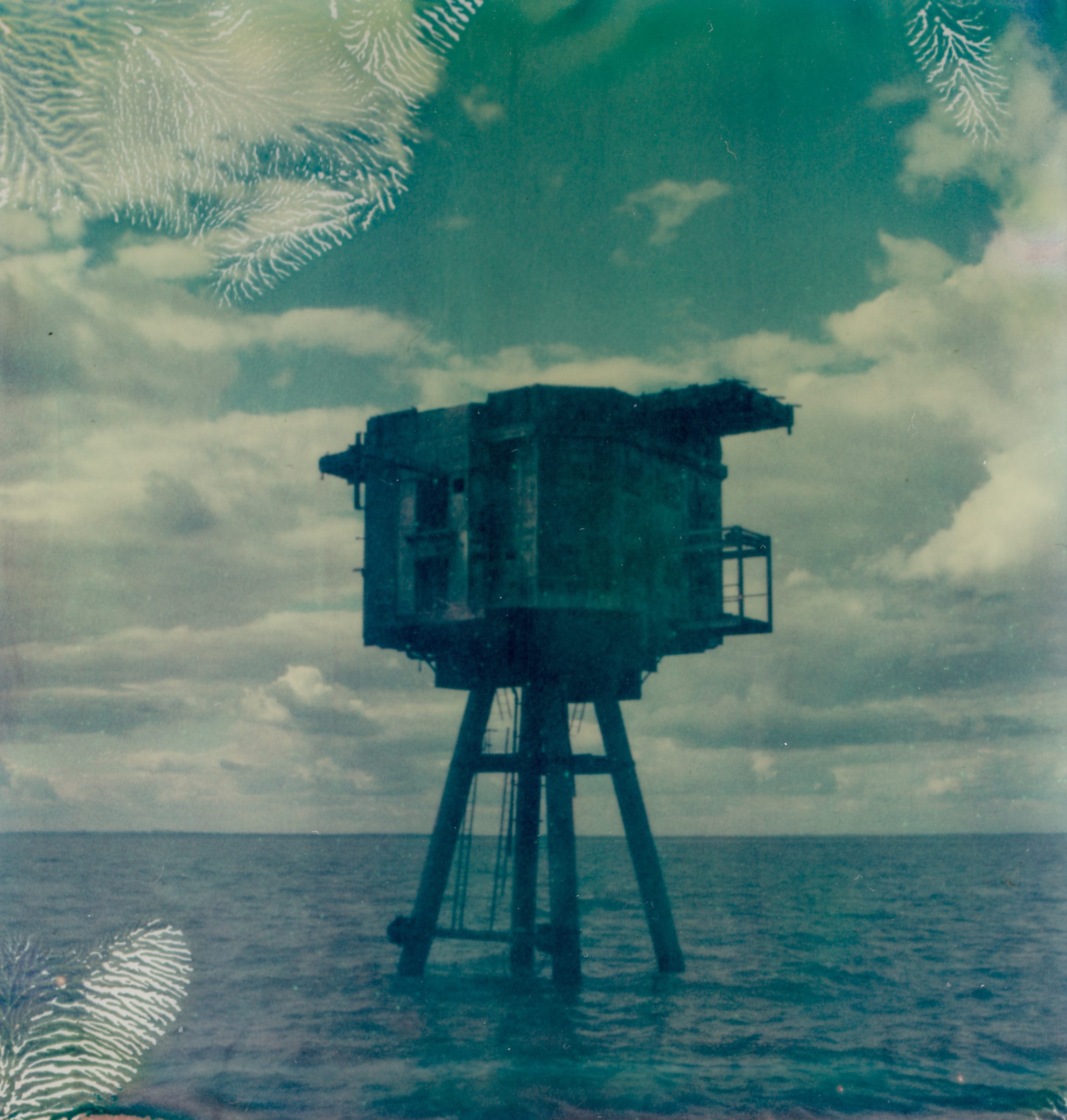 An abandoned sea fort stands on stilts above calm ocean water under a cloudy sky, captured beautifully by a photographer specializing in nighttime landscape photography.