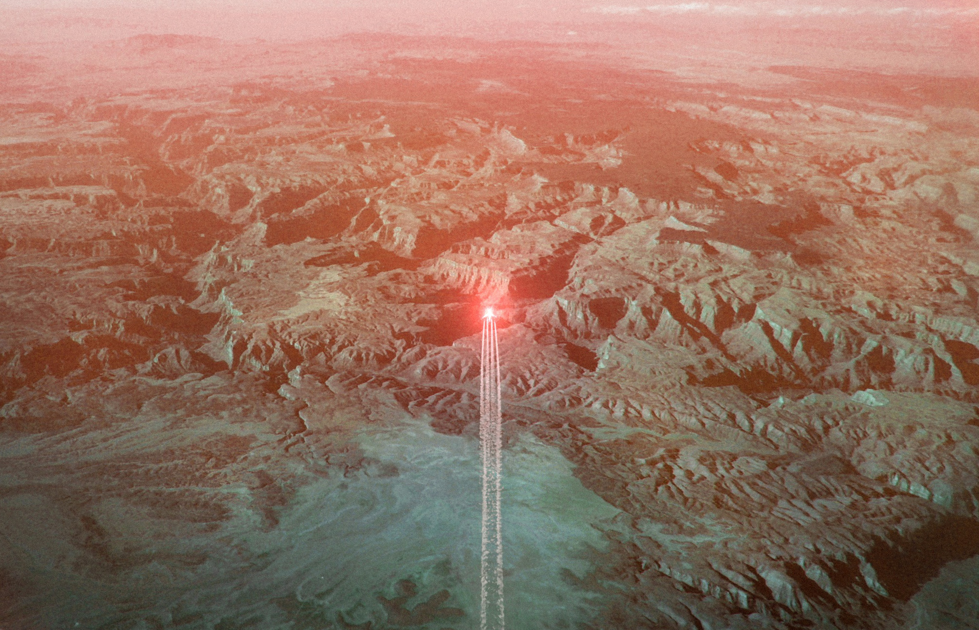 Aerial view of a desert landscape captured by a fine artist, featuring a jet with a bright red light at its nose leaving a vapor trail, evoking a futuristic atmosphere.