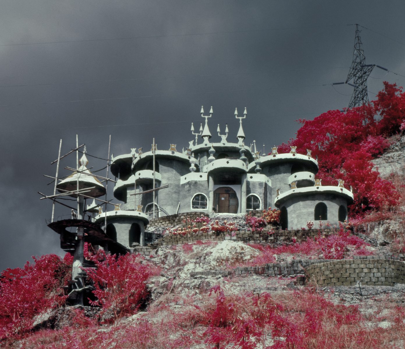 A whimsical, round-towered building sits on a hill amid vibrant pink foliage under a dark, cloudy sky, evoking the wonder of nighttime landscape photography.