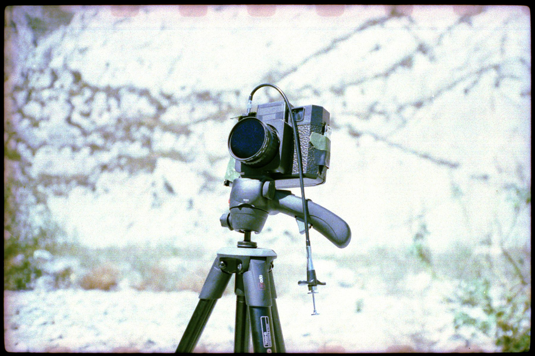 A vintage film camera on a tripod outdoors with a cable shutter release attached, ready to capture mesmerizing drone light painting displays.