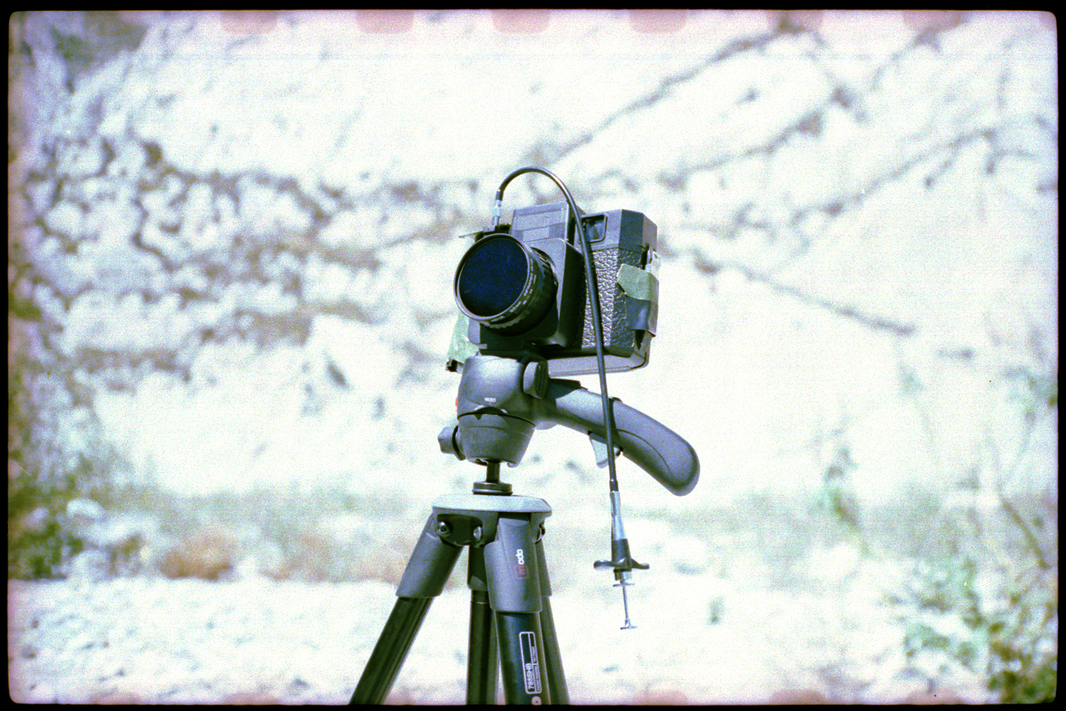 A vintage film camera on a tripod outdoors with a cable shutter release attached, ready to capture mesmerizing drone light painting displays.