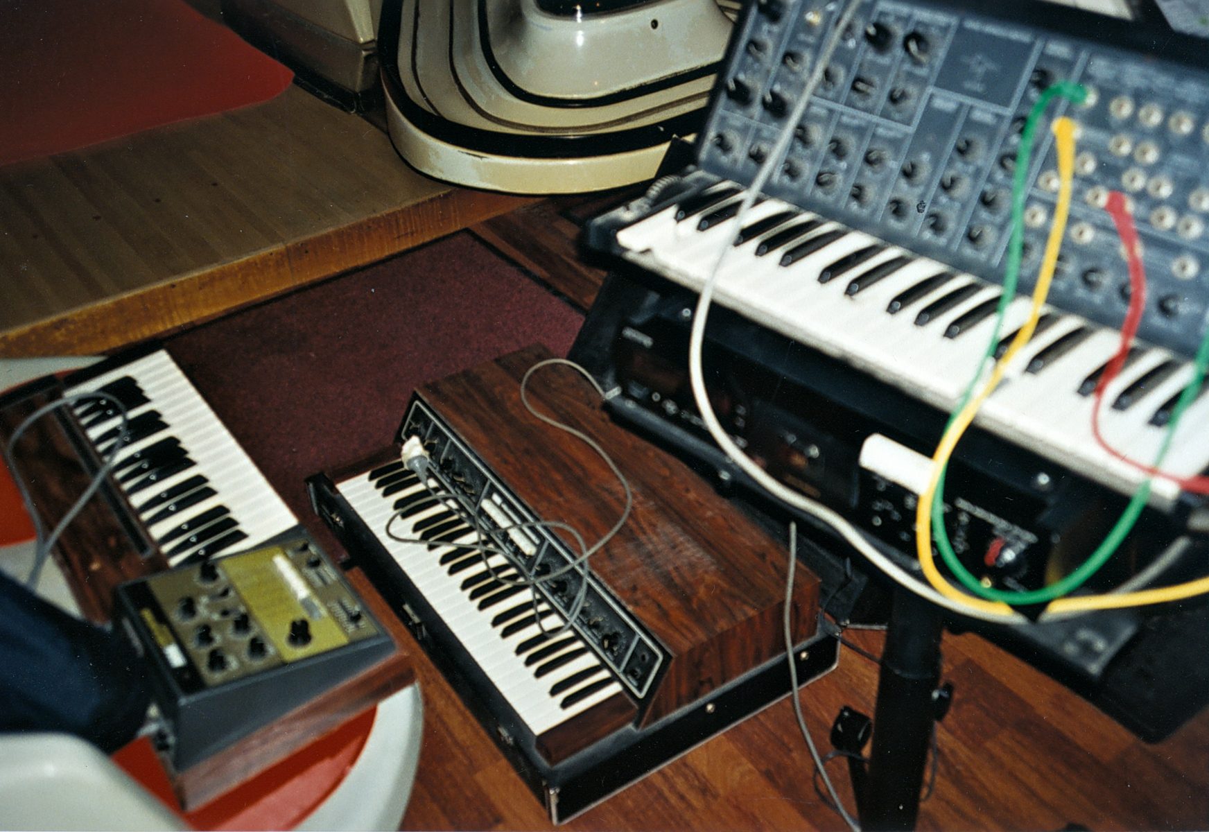 Three vintage synthesizers with patch cables and wooden panels arranged on a floor, wires visible—captured with the careful eye of a fine artist or photographer.