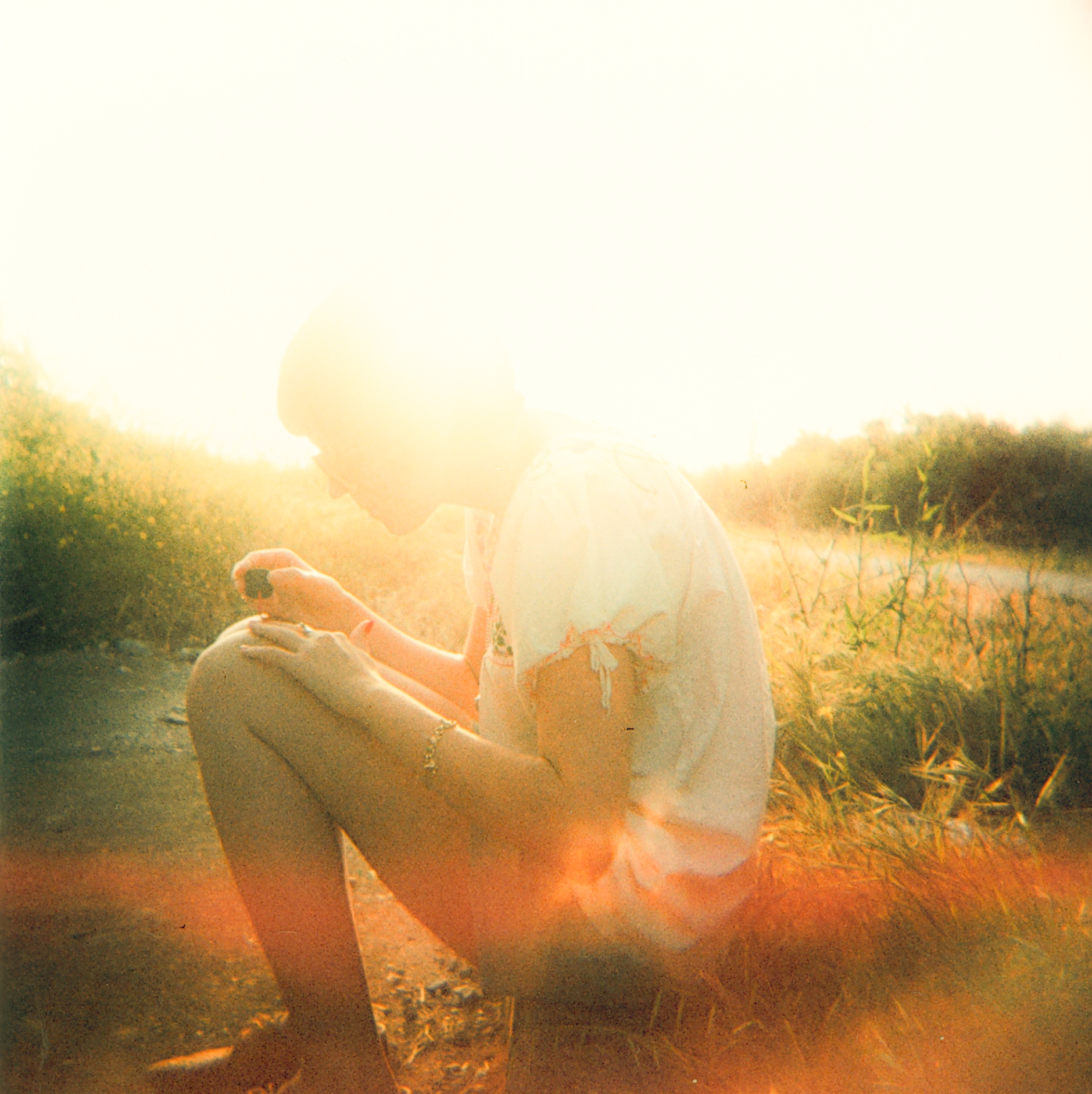 A person sits outdoors in bright sunlight, surrounded by grass and plants, with a warm, hazy glow—like a fine artist capturing nature's light or creating drone light art in the open air.