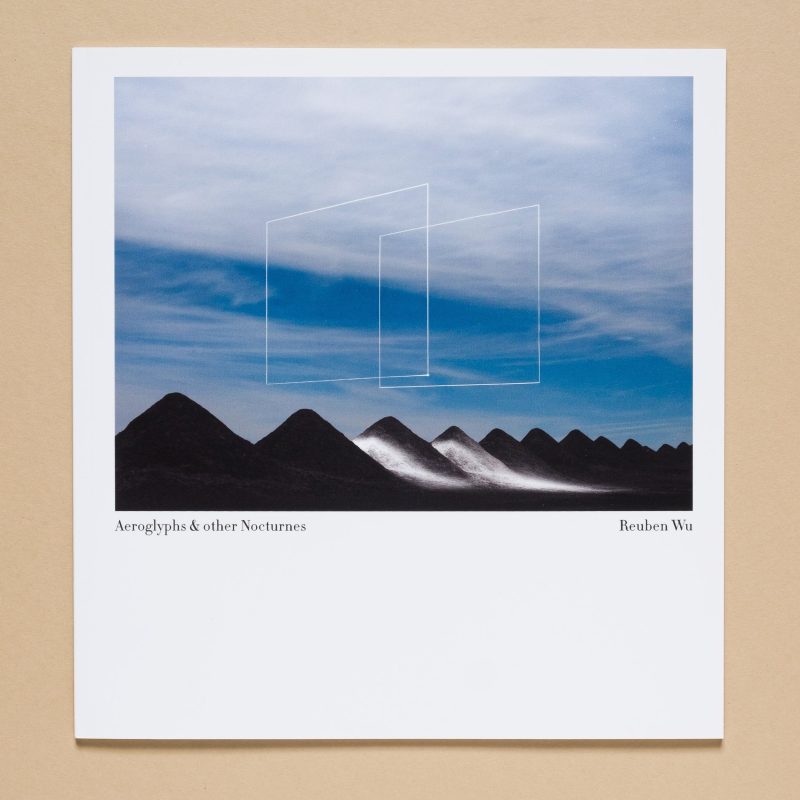 A photo of dark hills under a blue sky with white geometric lines—futuristic drone light art; text reads Aeroglyphs & other Nocturnes Reuben Wu.