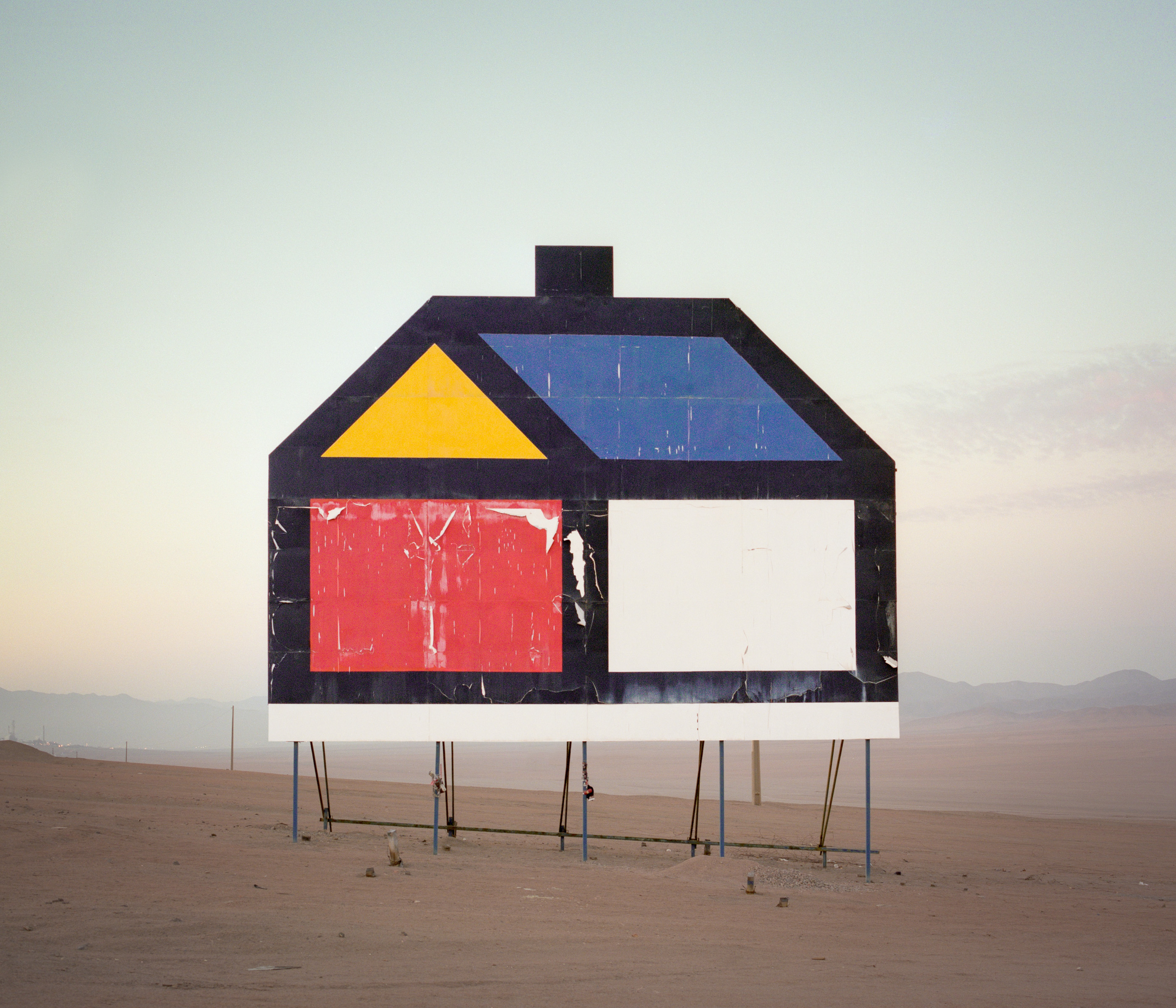 A large, abstract house-shaped billboard stands alone in a barren desert landscape at dusk, evoking a futuristic atmosphere perfect for nighttime landscape photography.