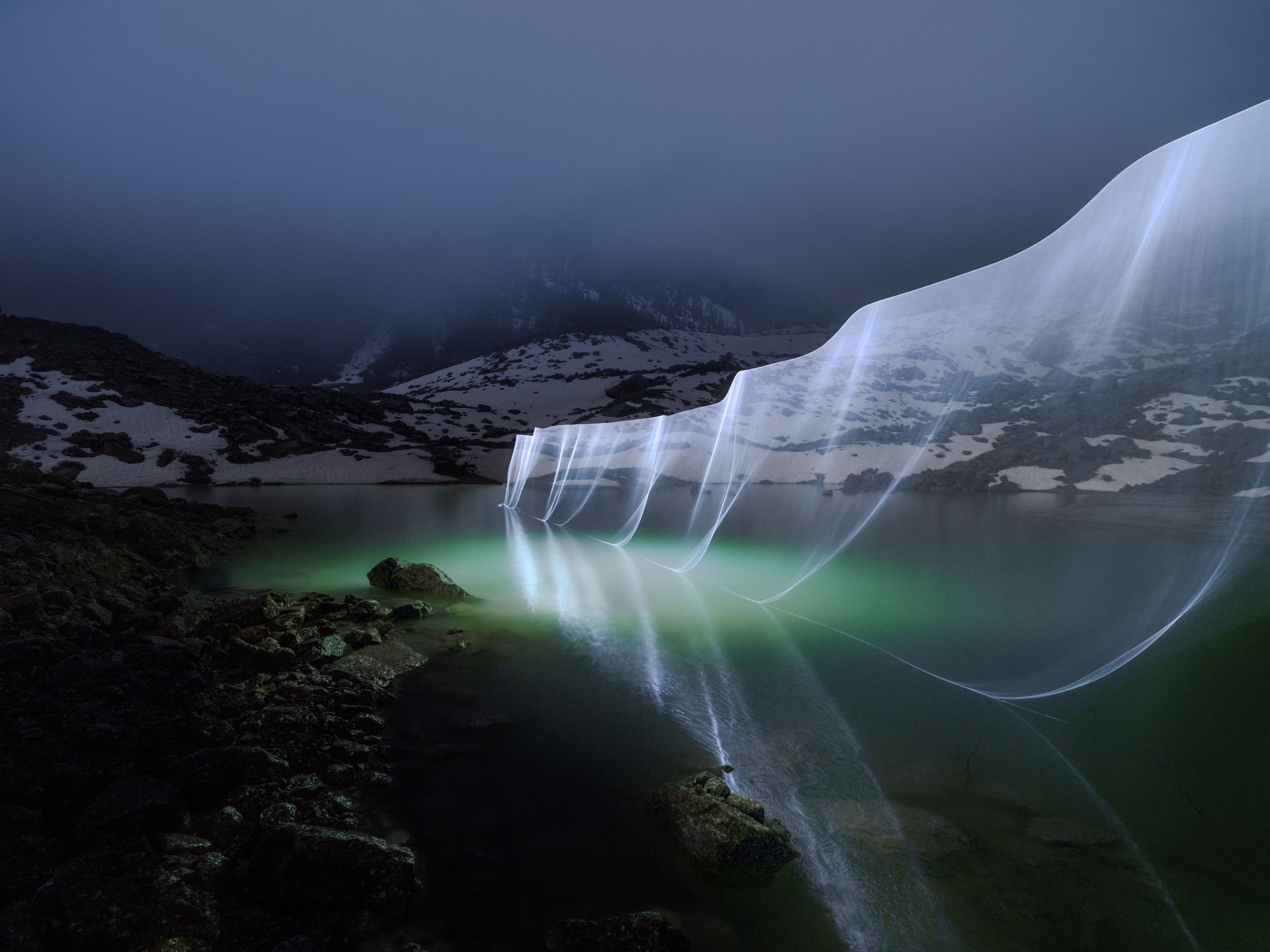 Snowy mountains by a lake at night, with a long-exposure light trail creating a glowing wave effect, evoke the magic of Skyway Monte Bianco under the starry sky.
